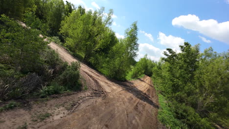 fpv drone flight low over dirt road and turning through trees on sunny day