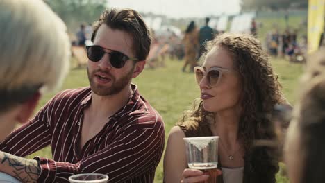 Eine-Gruppe-Von-Freunden-Sitzt-Beim-Musikfestival-Gemeinsam-Im-Gras-Und-Trinkt-Bier,-Während-Sie-Sich-Unterhält