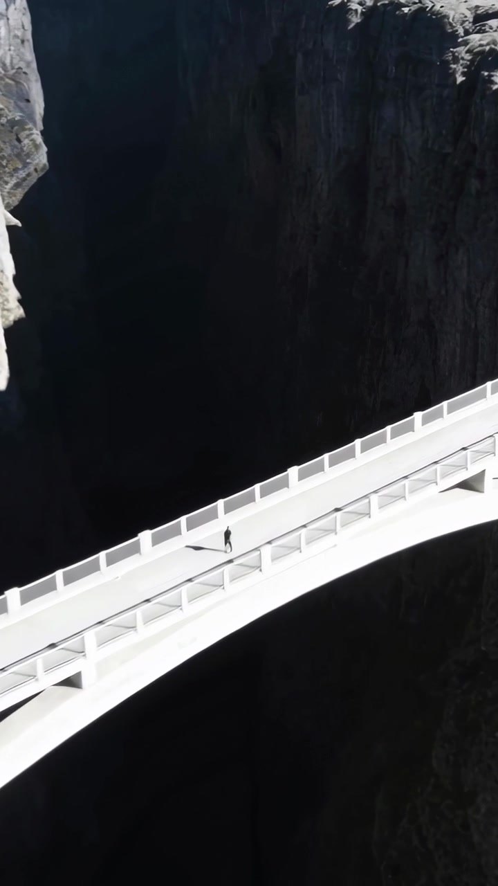 Video verticale: Drone che riprende un ponte bianco su una gola profonda, un escursionista in abiti scuri che cammina.