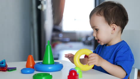 charming cute caucasian baby boy sits at the desk playing with pyramid. toddler puts on the colorful rings on hands and clapping hands cheerfully.