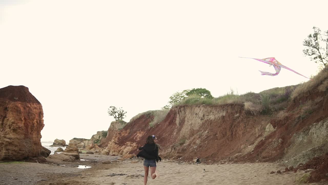 joven mujer hipster liberando una cometa colorida en la playa por la noche. disparo en cámara lenta