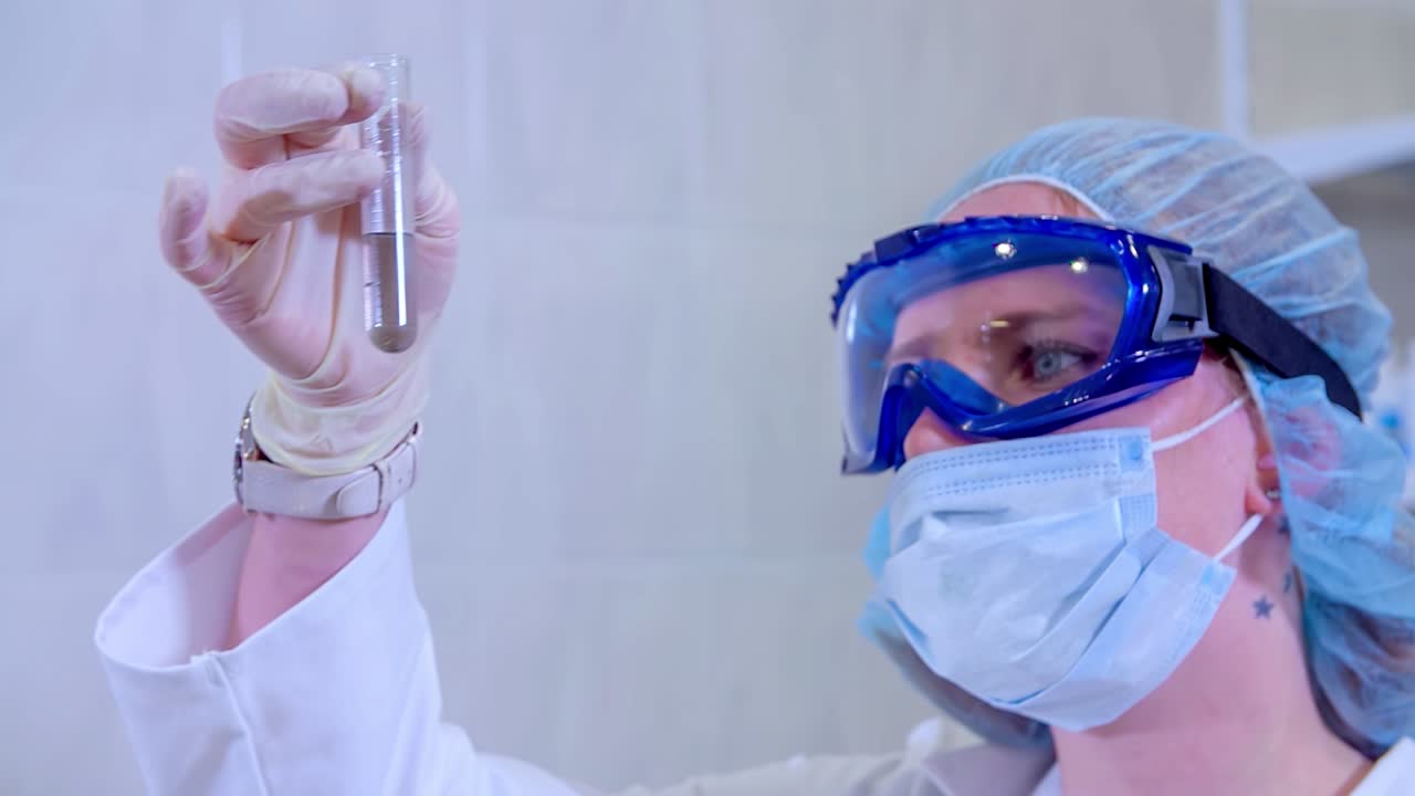 Scientist in protective gear examining a test tube in a lab