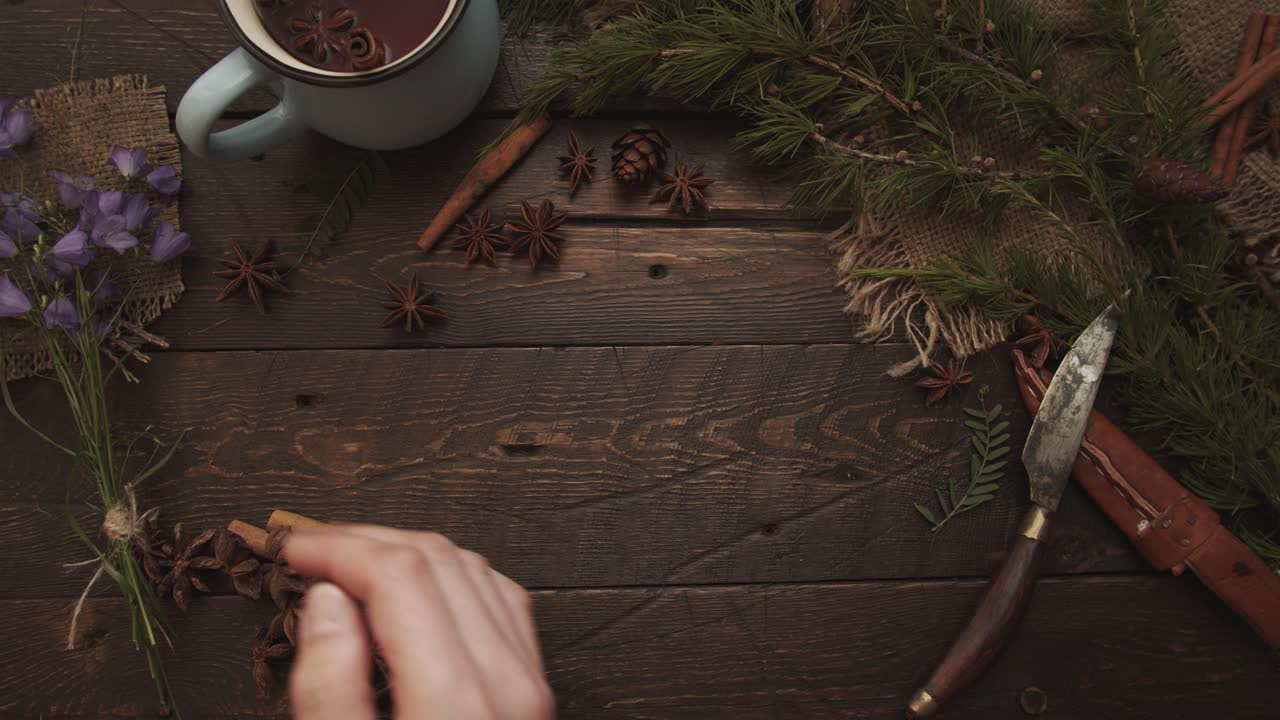 Hand Brushing away Star Anise on Rustic Table with Tea Mug and Pine Branches