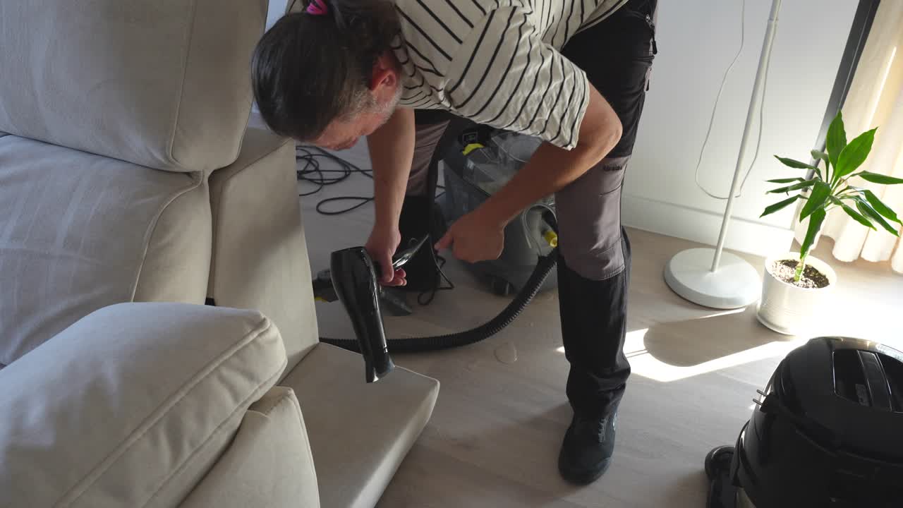 Top down shot of a male cleaner worker drying the fabric of the sofa with a hair dryer after using a special machine with ionized water