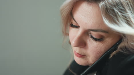 close up of professional woman holding phone between ear and shoulder during phone call, multitasking in quiet office environment with blurred background showing minimal movement