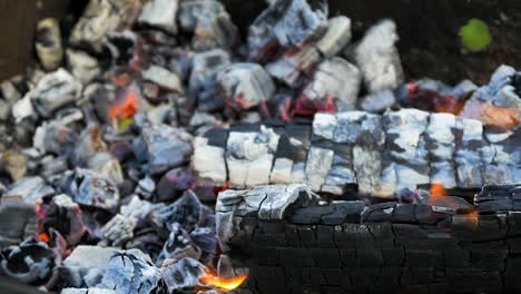 burning wood an coals in rusty portable outdoor bbq grill in sunny day, close up shot in slow motion