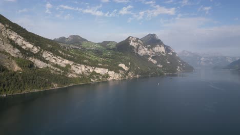 slow zoom in shot of a large water body in adjutant to the mountain peaks during the day with clear sky and clouds