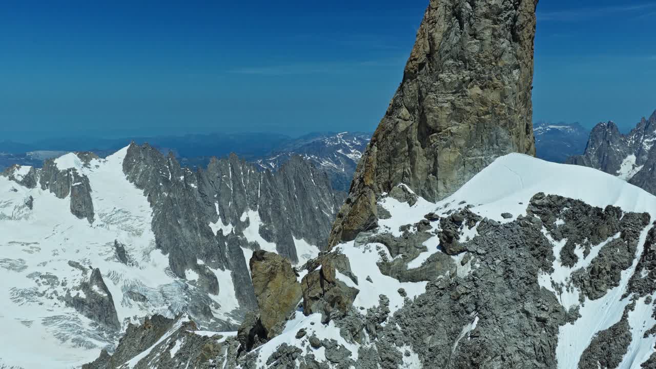 Ripresa aerea rivelatrice di un drammatico picco roccioso nelle Alpi francesi vicino a Chamonix, che cattura la ruvida texture del granito e il vasto paesaggio innevato del massiccio del Monte Bianco