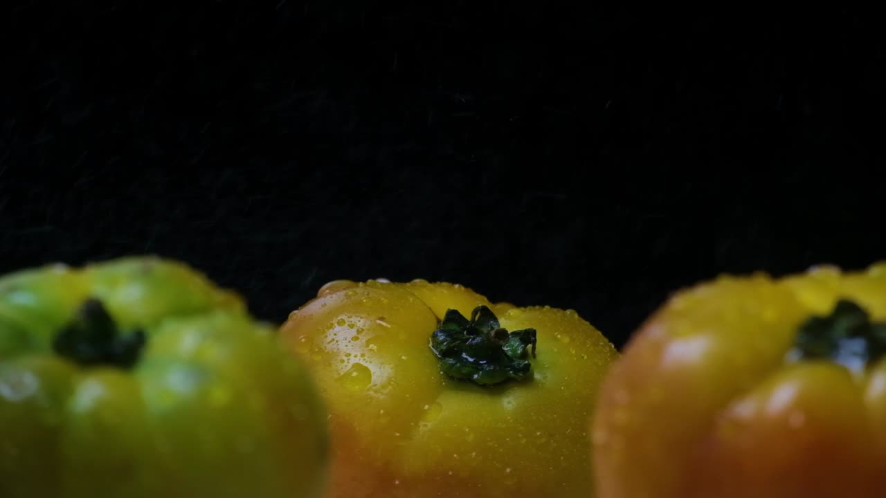 grandes tomates amarillos y verdes siendo salpicados desde el lado con agua, frente a un fondo negro
