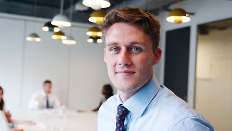 portrait of businessman in modern boardroom with colleagues meeting around table in background shot in slow motion