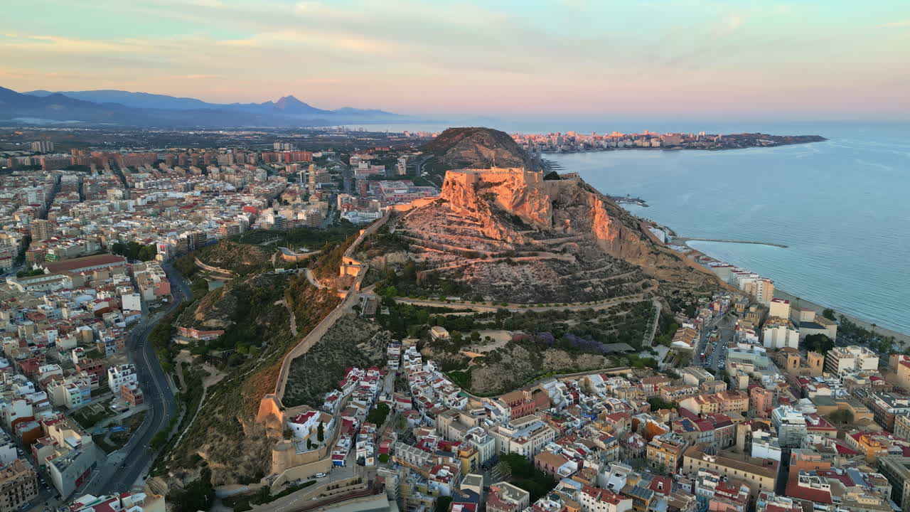 Aerial drone view of the Santa Barbara Castle surrounded by buildings on the coast of Alicante, Spain with the sea on the background