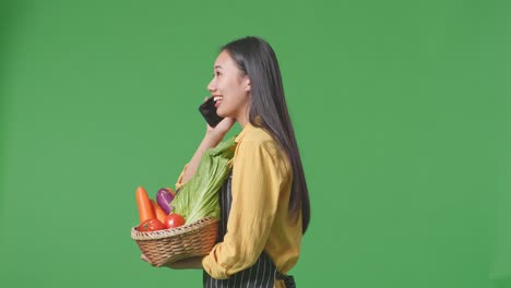 woman talking on phone while holding a basket of vegetables