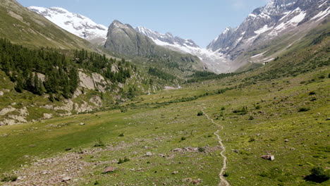 Vista-Aérea-Avanzando-A-Través-De-Un-Valle-De-Montaña-Con-Montañas-Nevadas-En-El-Fondo,-En-El-Verano