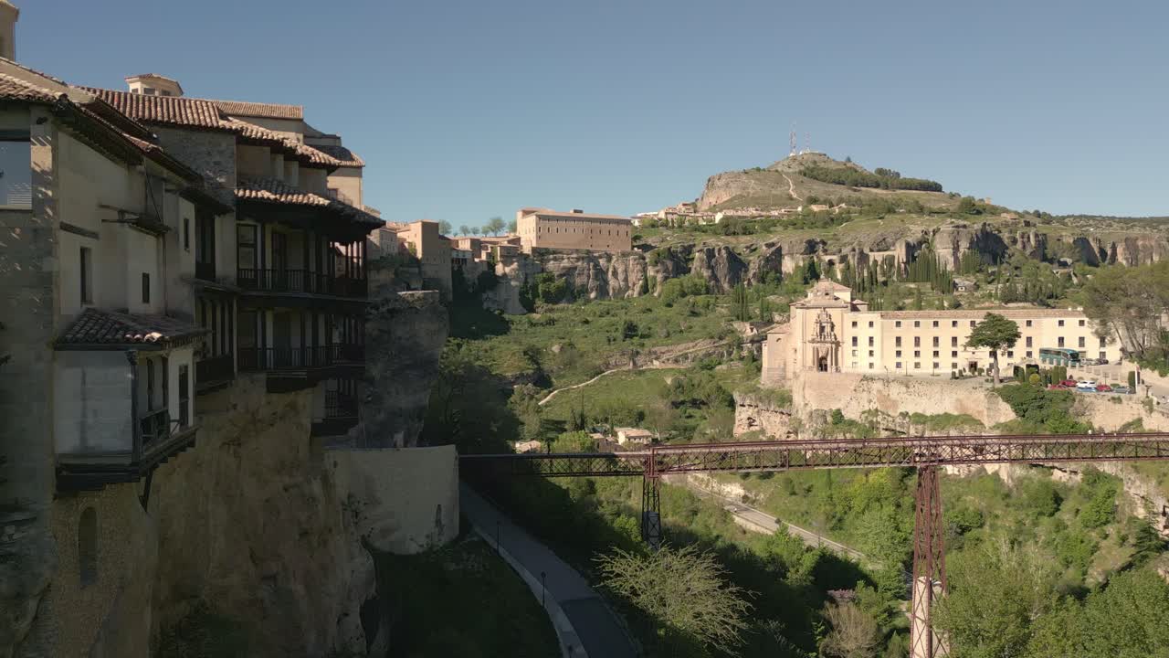 Houses hanging next to rocky precipice bridge and church. Travelling aerial view of medieval houses next to a cliff. Cuenca. Spain.