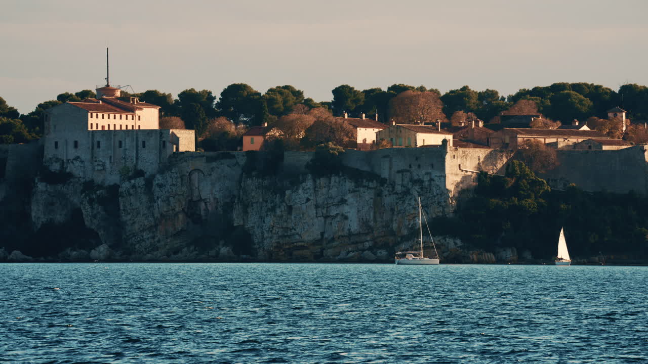 Barca a vela che galleggia sulle calme acque del Mediterraneo di fronte allo storico Fort Carré ad Antibes