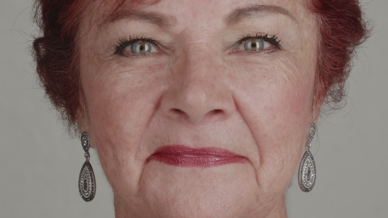 High-quality 4K footage of a confident senior woman (60s-70s) with styled hair and jewelry, looking straight into the lens with a soft, friendly smile. Excellent for mature beauty, retirement