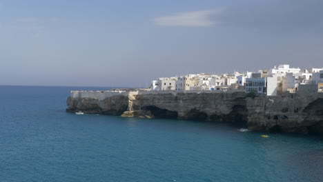 Toma-Estática-De-La-Costa-De-Polignano-A-Mare,-Barco-Navegando-En-Aguas-Azules