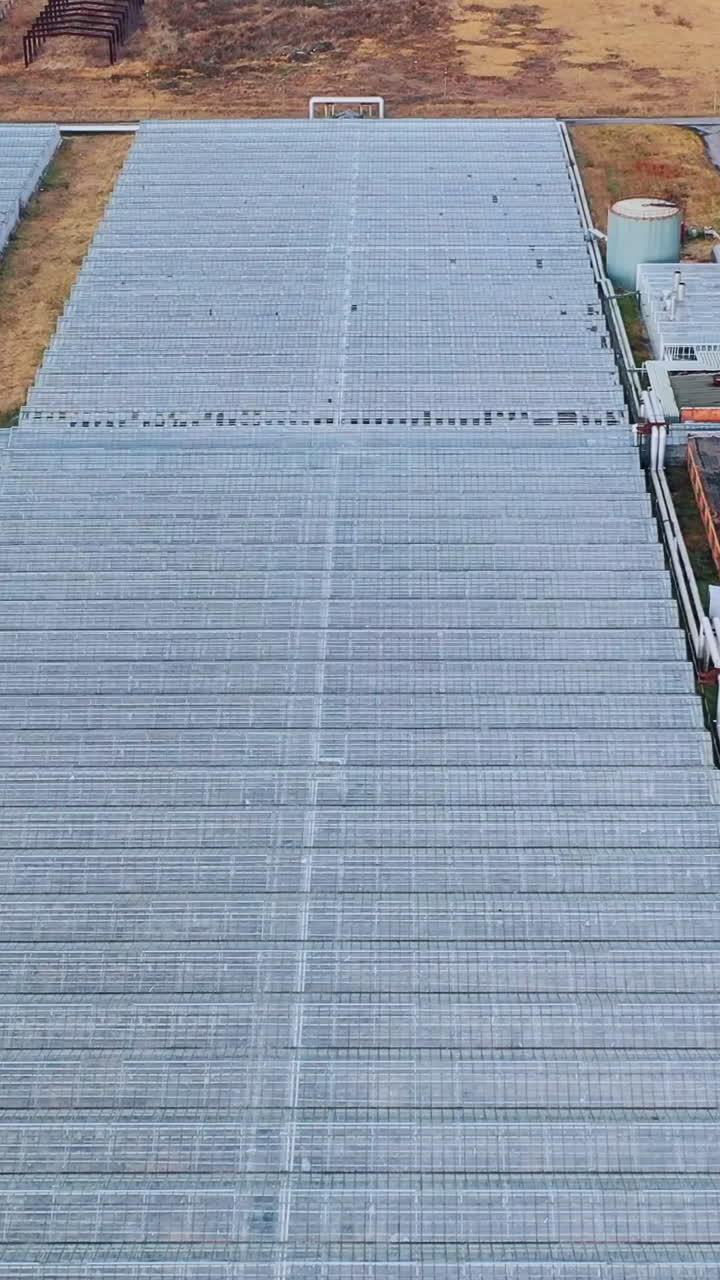 Large glass greenhouses with utilities and heating systems. Agriculture all year round. View from above. Aerial View. Vertical video