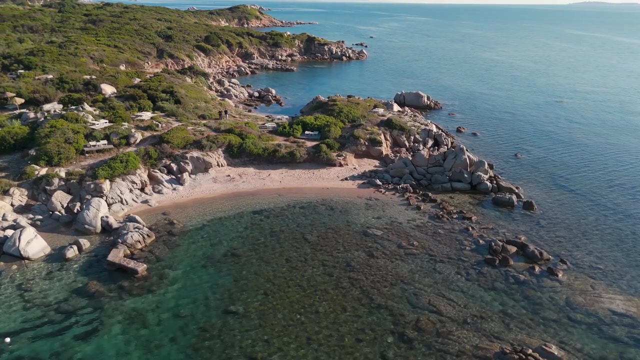 Luftaufnahme einer felsigen Küste und einer klaren türkisfarbenen Bucht mit Sandstrand im Sonnenlicht