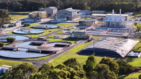 aerial camera pans across a modern wastewater treatment plant surrounded by greenery, showing water tanks, buildings, and infrastructure in bright daylight