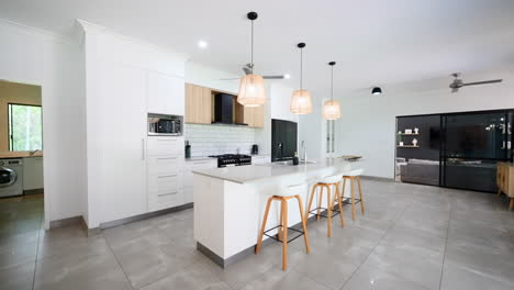 modern luxurious tropical home interior kitchen with rattan chairs and stools around sleek grey black appliances