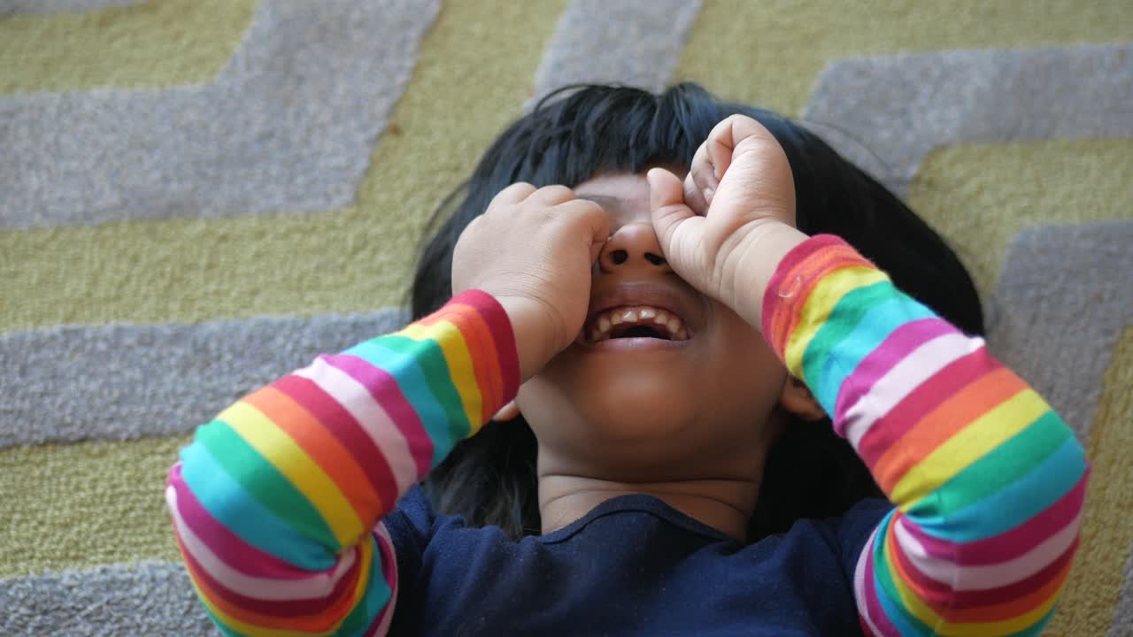 una niña riendo y cubriendo sus ojos con su mano