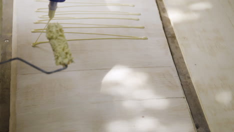 close-up of glue bottle moved in a zigzag pattern on a wooden board with a spreader held at the ready