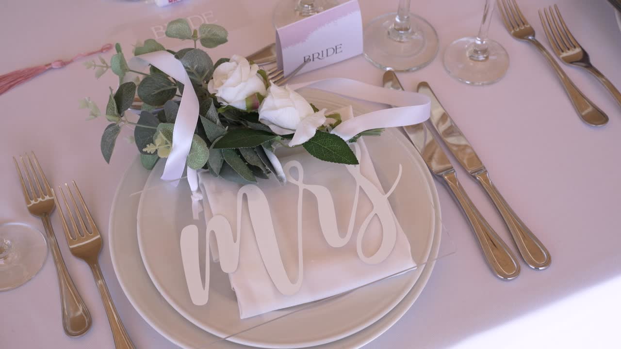 La tavola, elegantemente apparecchiata, mette in mostra un delicato centrotavola floreale, un segnaposto personalizzato ed eleganti accessori da pranzo, creando un'atmosfera romantica per un ricevimento di matrimonio.