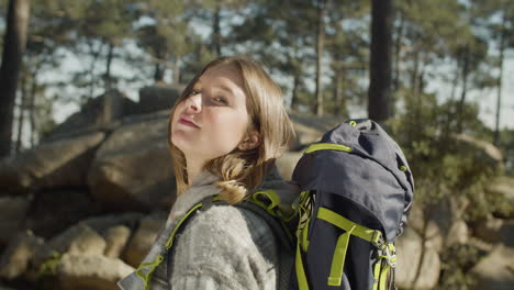 portrait of a brown haired female backpacker looking at the camera while hiking in the forest on a sunny day 1