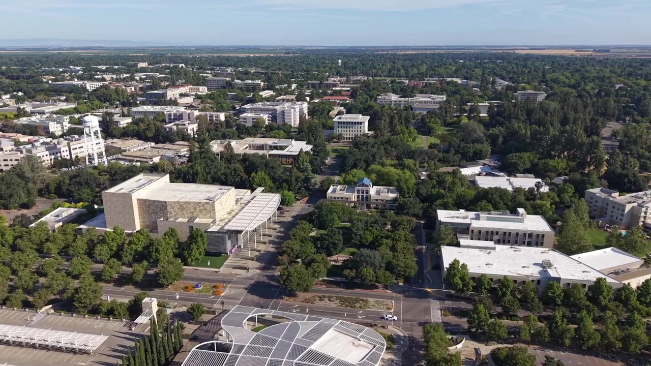 Luftperspektive, die den weitläufigen Campus der University of California, Davis, zeigt und dessen moderne Architektur, üppige Grünflächen und akademische Gebäude an einem klaren sonnigen Tag hervorhebt.