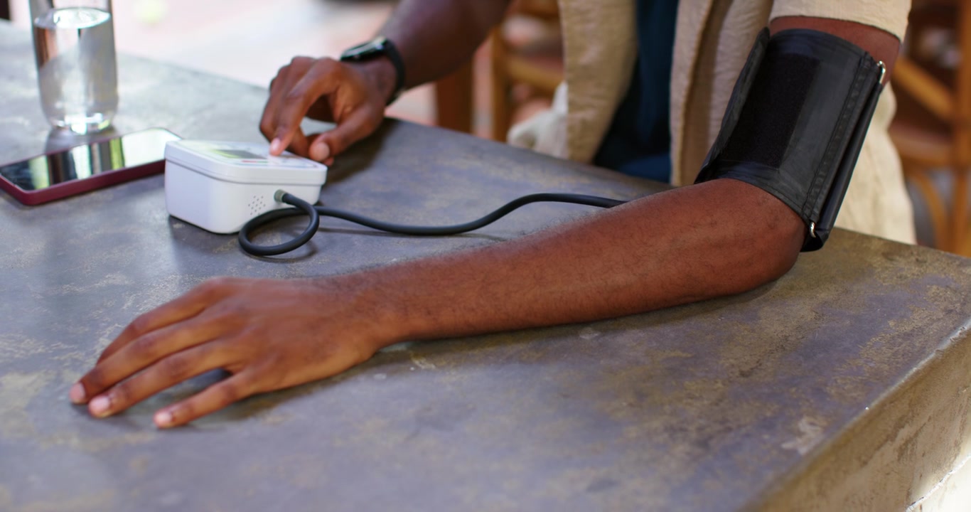Uomo afroamericano che si prepara per il controllo della pressione sanguigna, avvolgendo il bracciale sul braccio destro sul bancone, premendo il monitor.