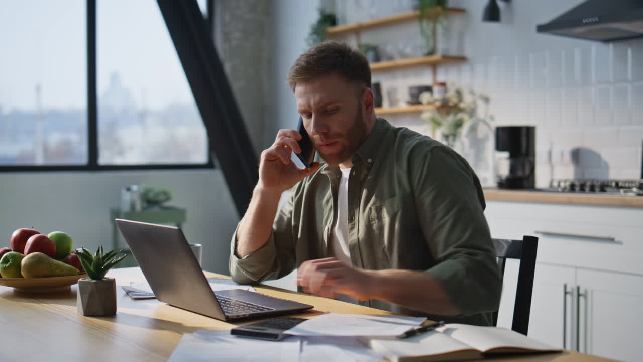 Tænksom administrator taler i telefon og arbejder på bærbar computer på hjemmekontoret tæt på