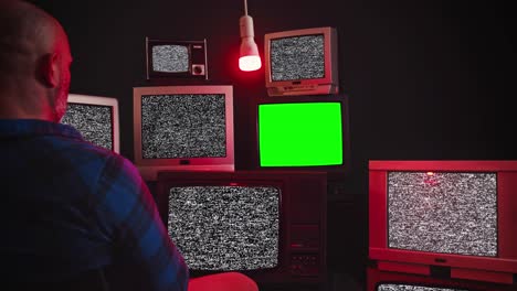 a man sits in front of group of 9 vintage tv with chroma key screens in room with black wall