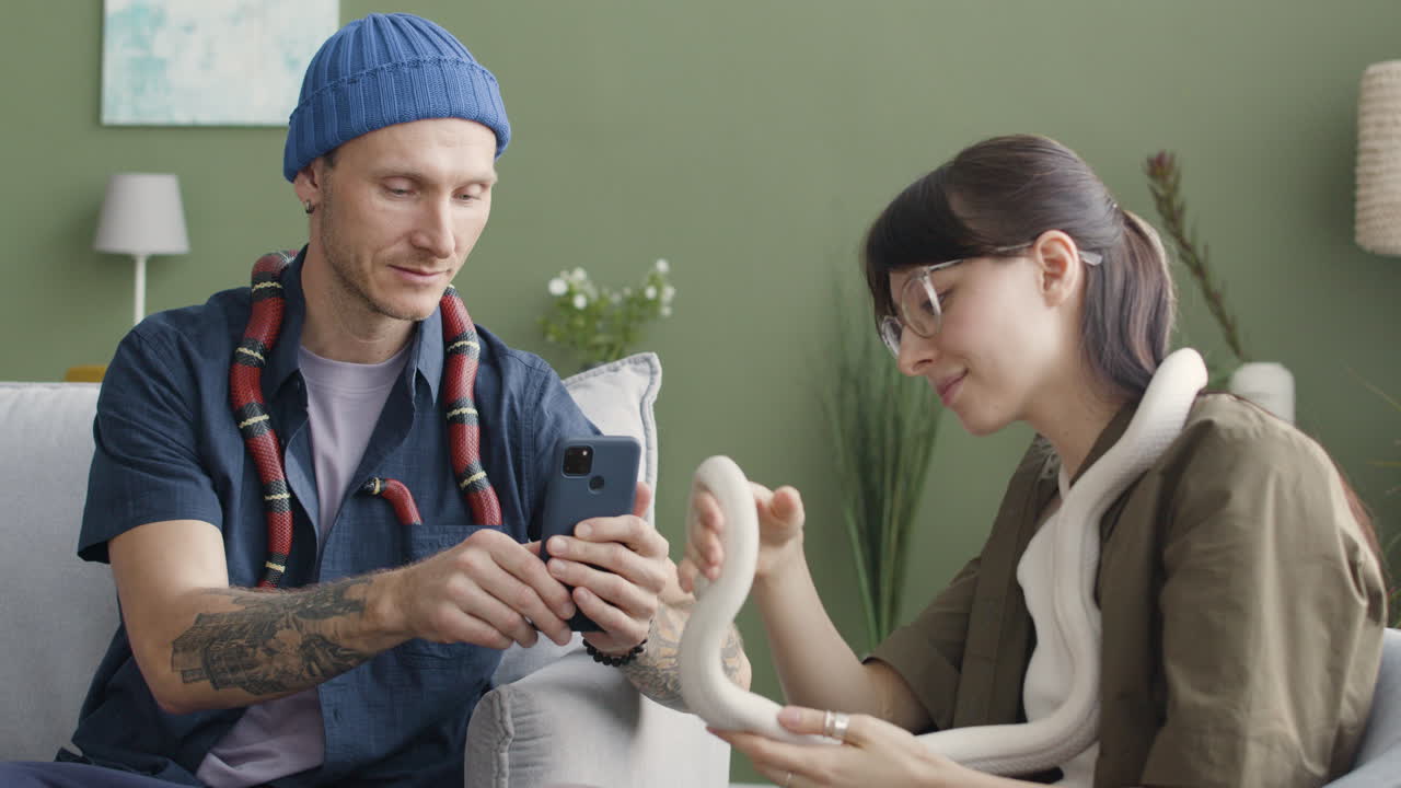 pareja sosteniendo serpientes mascota sentadas en un cómodo sofá en casa 1