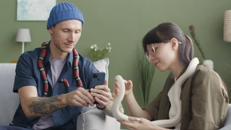 Couple-Holding-Pet-Snakes-Sitting-On-A-Comfortable-Sofa-At-Home-1