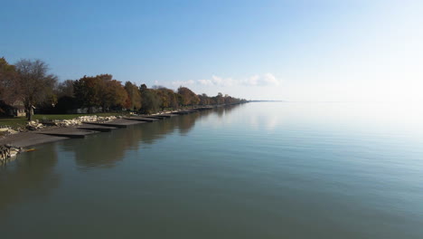 aerial dolly along peaceful early morning lakeside water homes and erosion control barries of lake erie