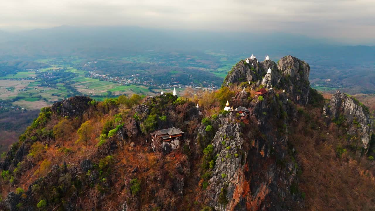 Mountain ridges crowned with hilltop shrines at Wat Chaloem Phra Kiat in Thailand at sunrise, aerial