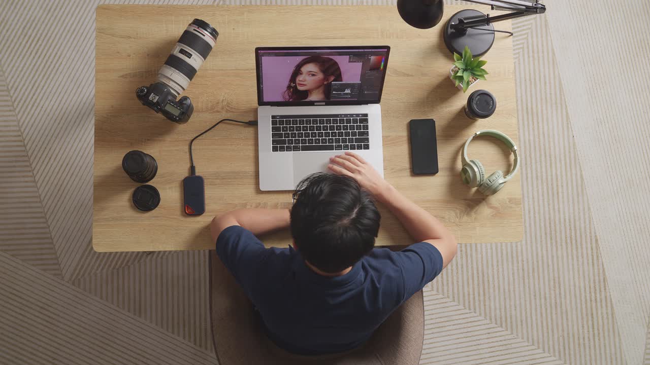 Top View Of Asian Male Editor Having A Backache While Sitting In The Workspace Using A Laptop Next To The Camera Editing Photo Of A Female At Home