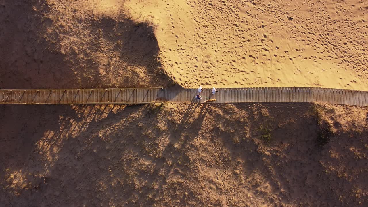 gente caminando con perro a lo largo de un puente peatonal de madera en la playa al atardecer, punta del este en uruguay
