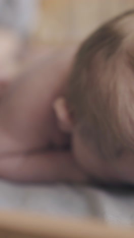 small newborn baby with short blond hair lies on stomach and pediatrician makes back massage close view