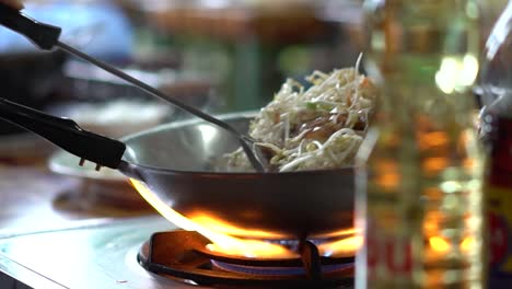 Person-Cooking-Pad-Thai-in-a-Wok-on-a-Stove-High-Heat-in-an-Outside-Kitchen-in-Bangkok-Thailand-SLOW-MOTION