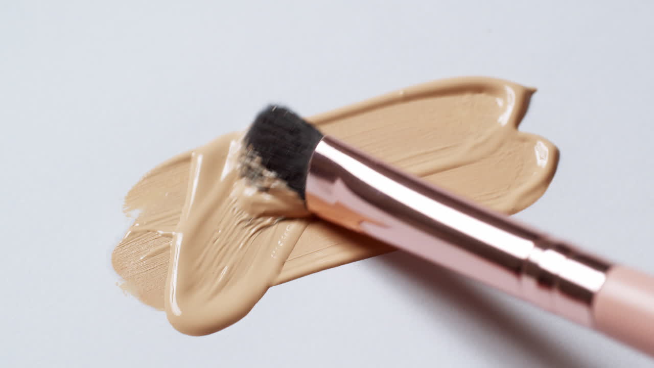 cepillando una capa de base de maquillaje en una tabla de paleta blanca y limpia para comprobar su textura y tono