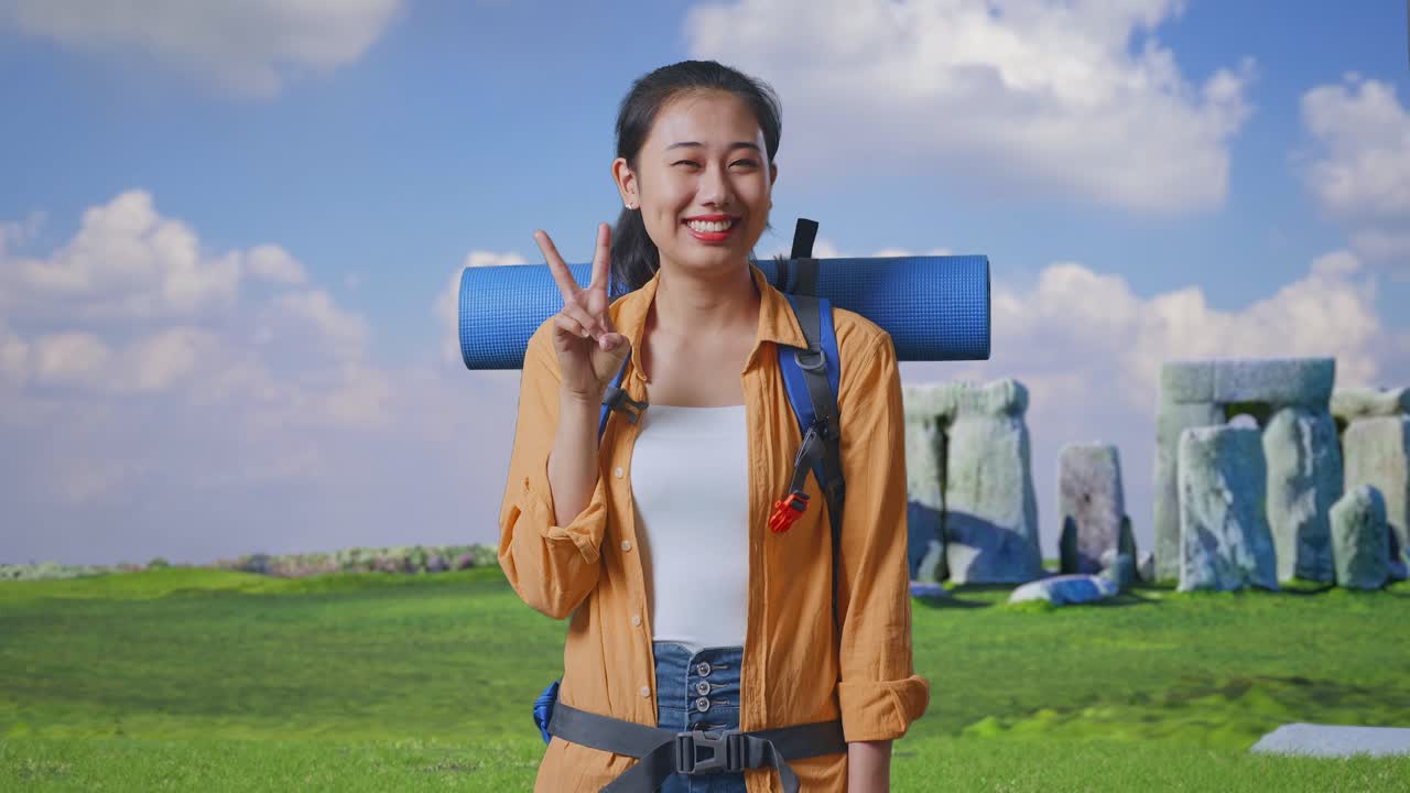 Asian Female Hiker With Mountaineering Backpack Smiling And Showing Peace Gesture While Traveling In Stonehenge