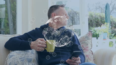 animación de conexiones y globo sobre hombre caucásico bebiendo café y usando teléfono inteligente
