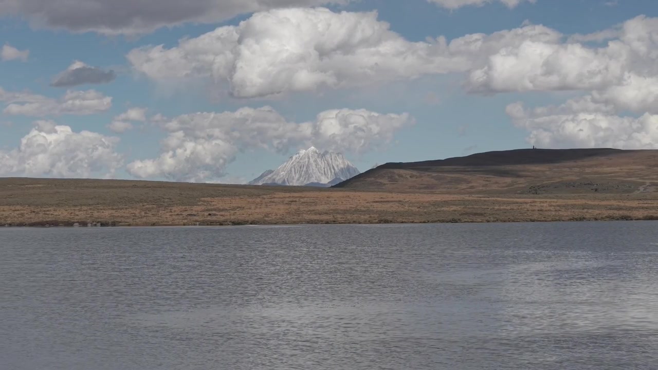 Calm lake with distant snow capped mountain beyond open moorland beneath dramatic clouds. Peaceful natural scenery in Scotland United Kingdom during daytime