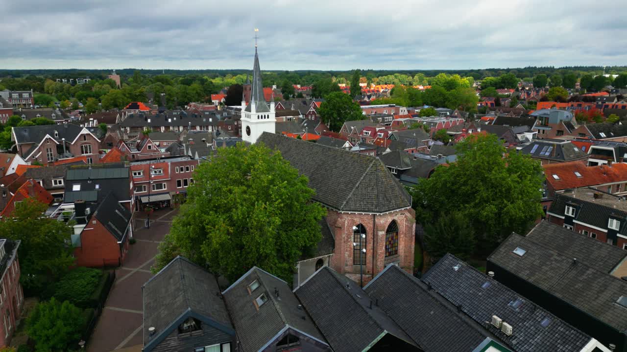 Drone shot of Ommen’s historic church and rooftops with white tower rising above brick houses and green trees. Location: Ommen, Overijssel, Netherlands (Ommen, Overijssel, Nederland