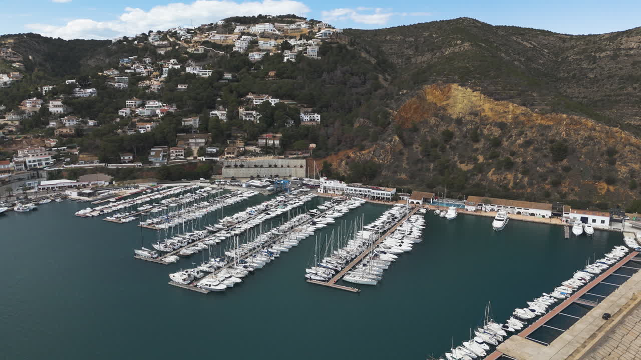 Curved harbor infrastructure wraps around tightly grouped boats in Spanish marina