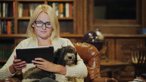 a woman relaxes in a luxurious home library holds a small dog