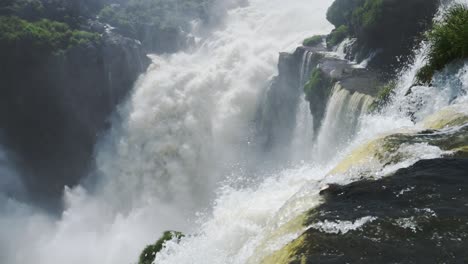 high up view of wide river falling from huge cliff, tall large waterfall dropping off steep edge in rocky rainforest scenic location in iguazu falls, argentina, south america