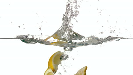 Lemon-segments-plunging-into-water-on-white-background